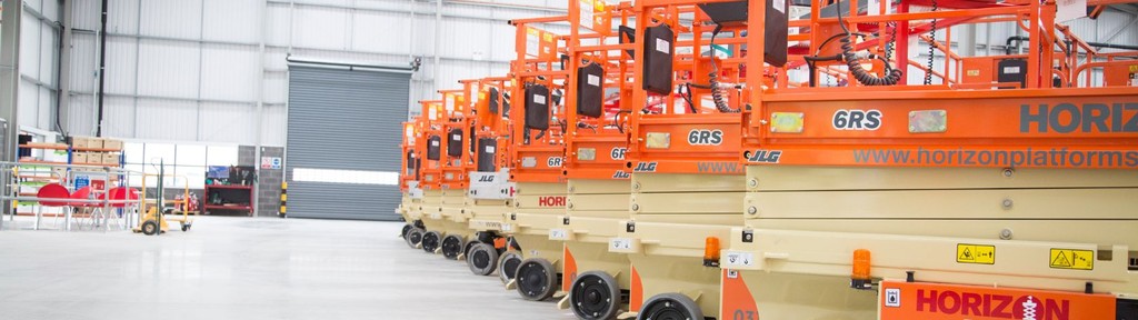 A row of clean scissor lifts inside big warehouse waiting to go on hire